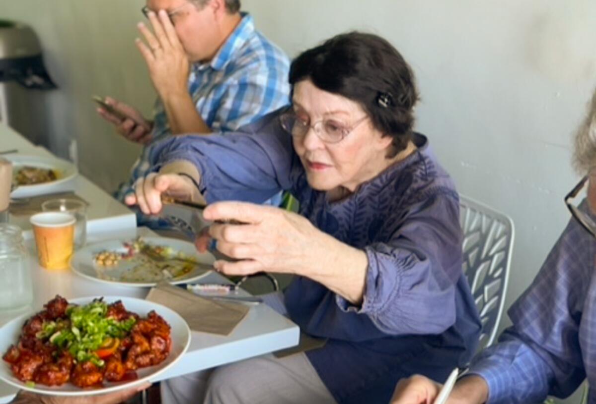 A woman seated at a restaurant table takes a picture of a plate of food.