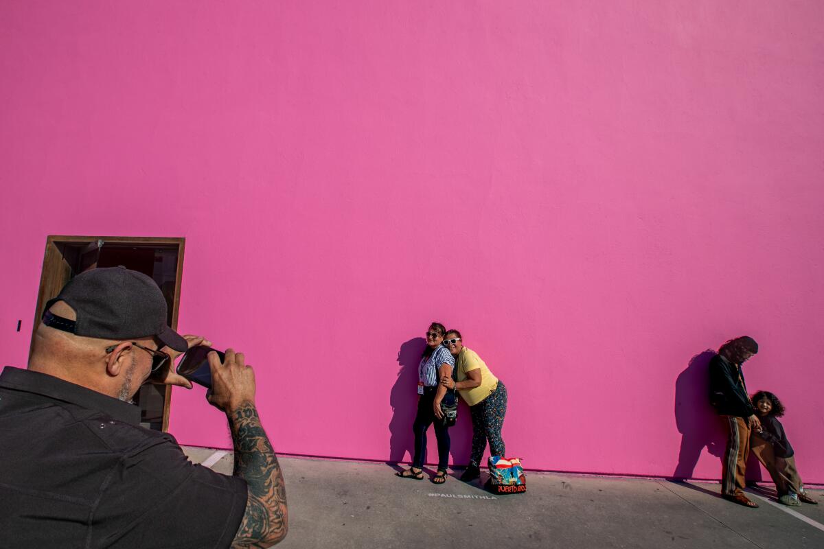 People taking pictures in front of a vibrant pink wall outside.