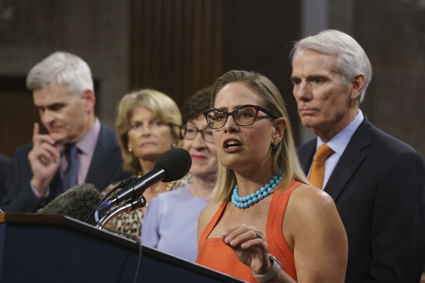 Sen. Kyrsten Sinema speaks at a lectern while other people stand nearby. 
