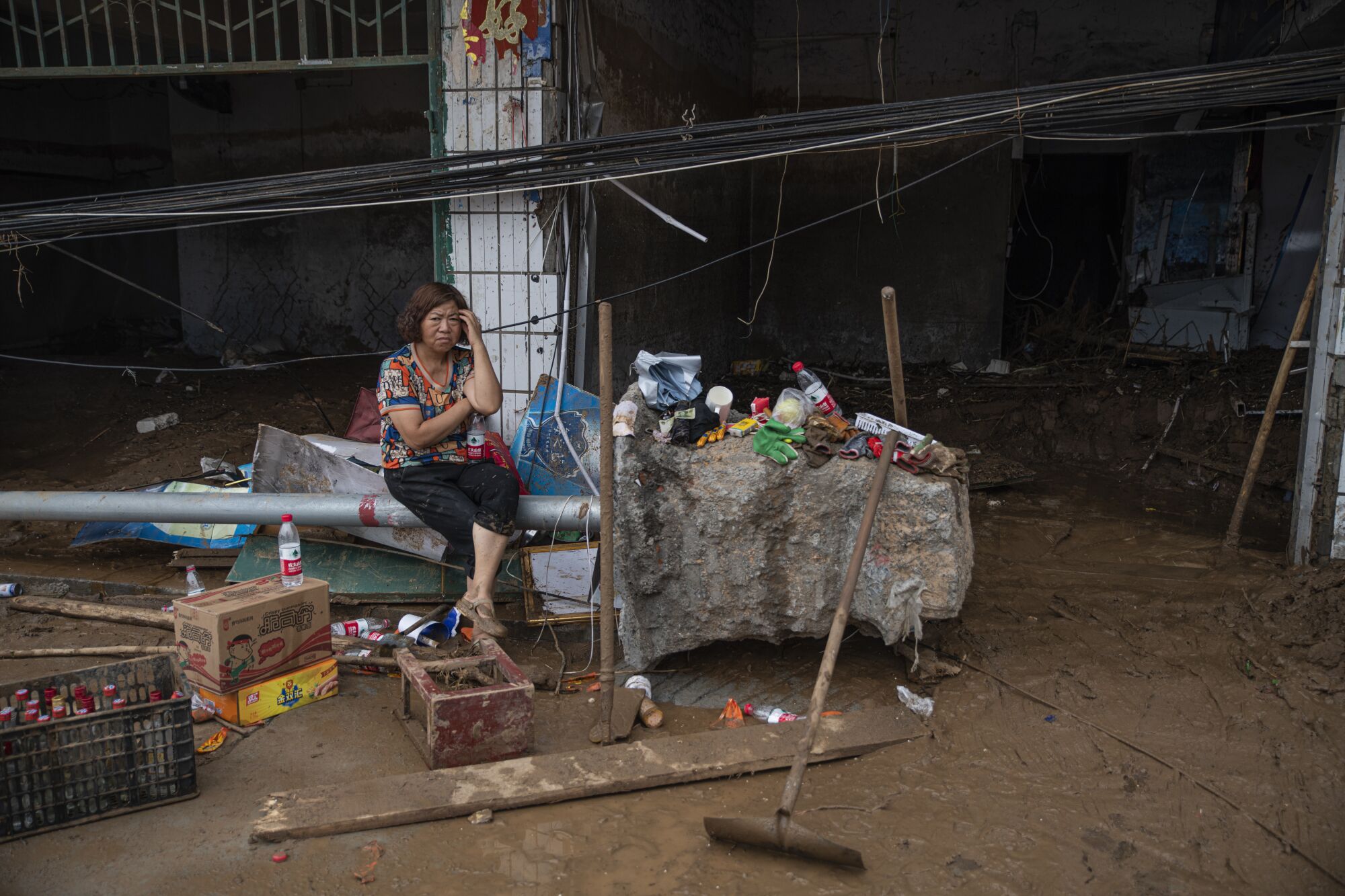 A woman sits amid mud and flood debris