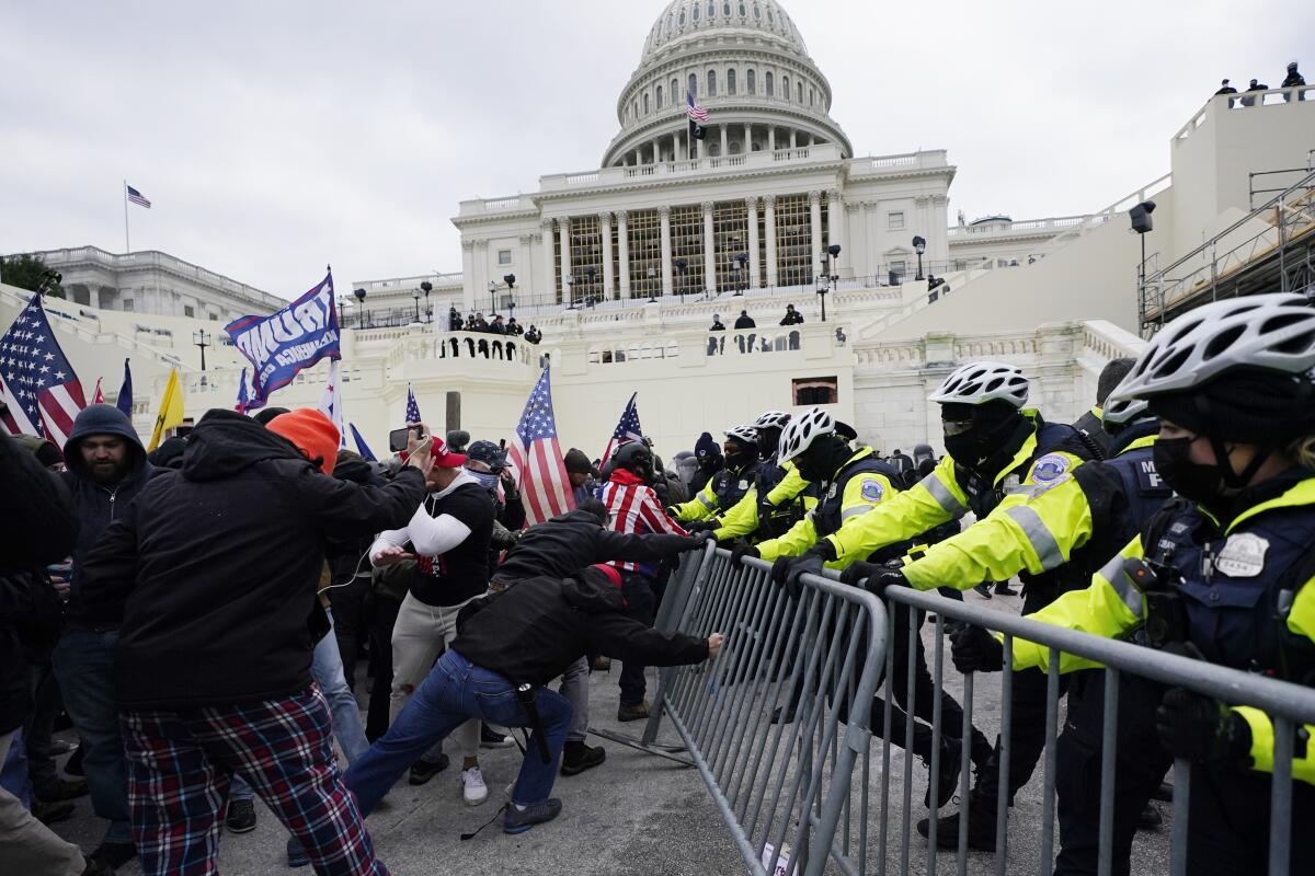 People with U.S. and Trump flags shove against a metal barrier as a line of police tries to hold them back.