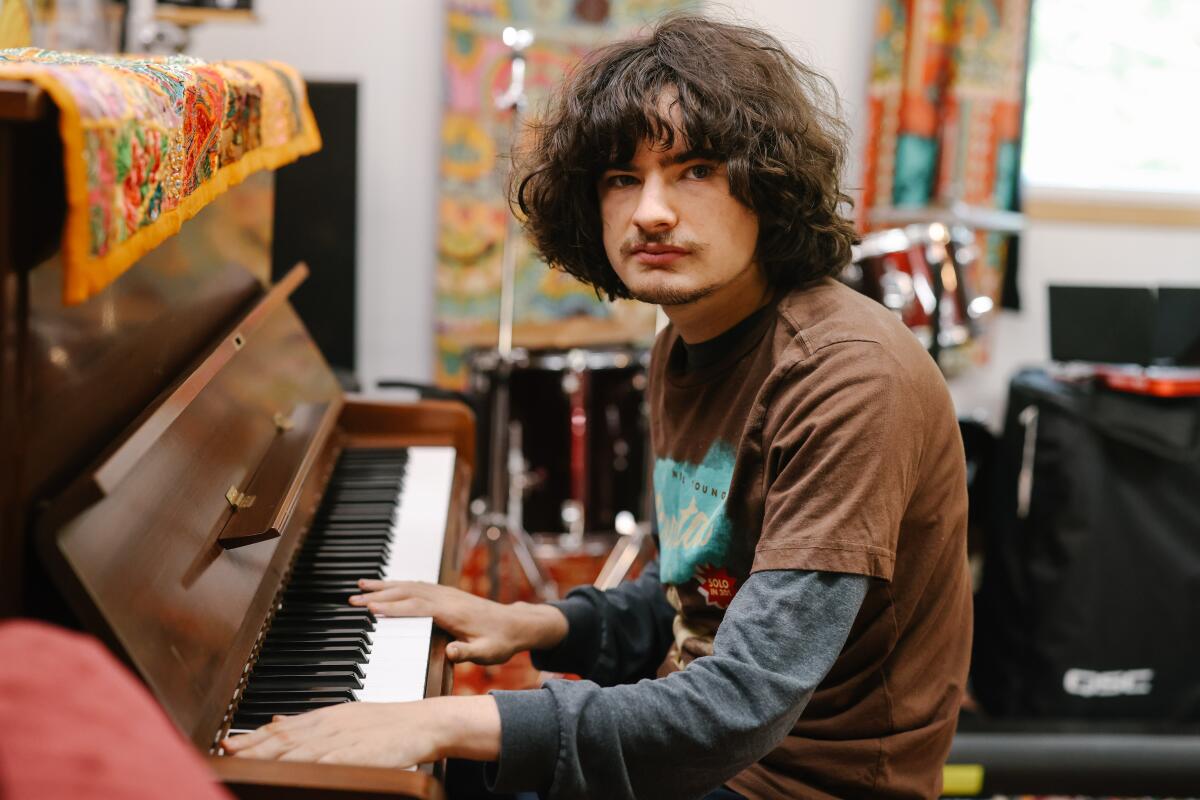 Jacob Rock poses for a portrait with his hands on a piano at his home studio.