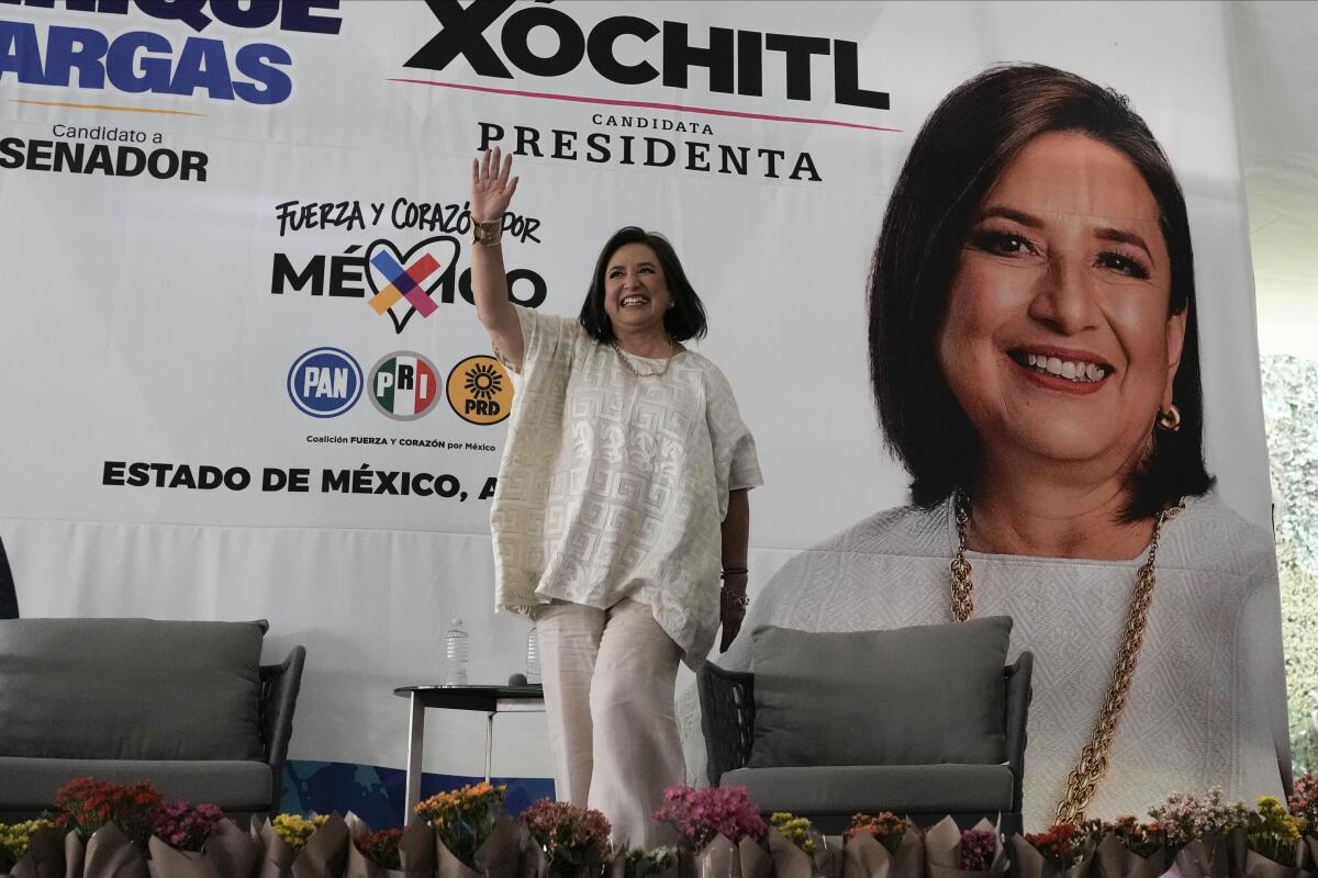     Xóchitl Gálvez saluda en un escenario frente a una pancarta con su imagen 