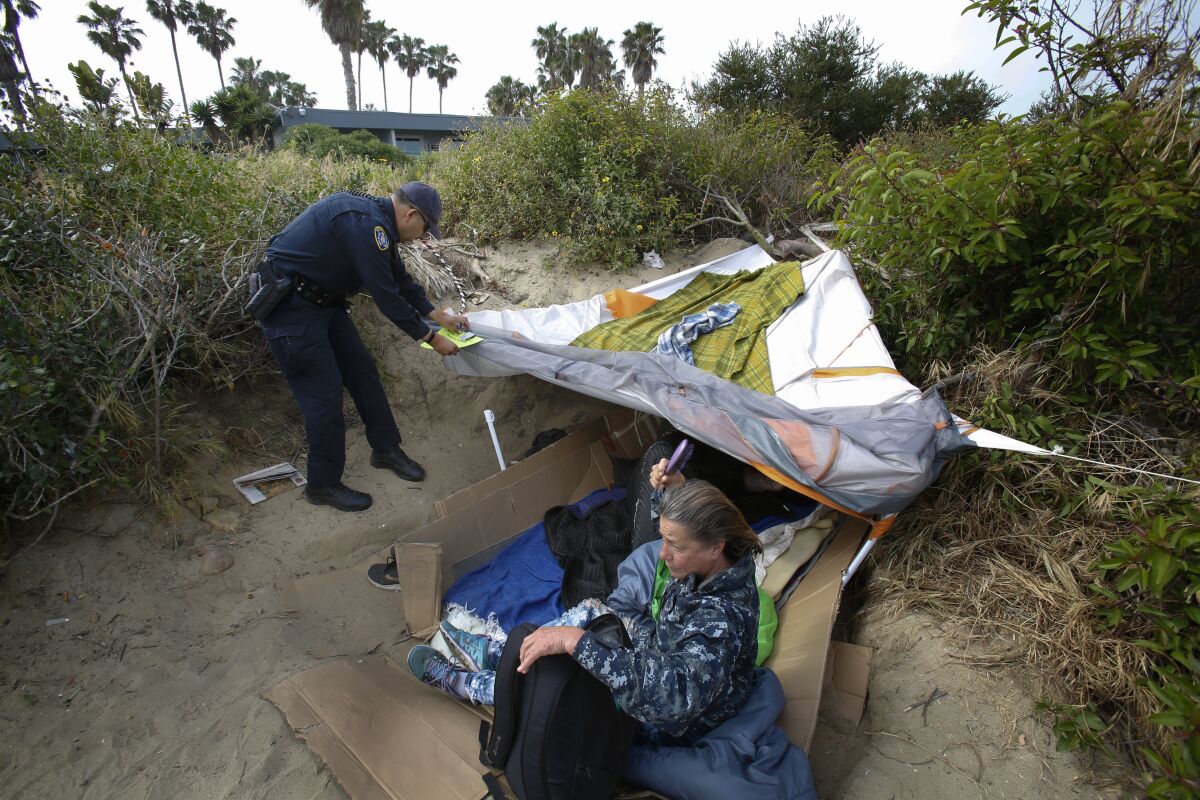 A San Diego police officer tapes a notice of cleanup to a tent belonging to a homeless couple in Ocean Beach in 2019.