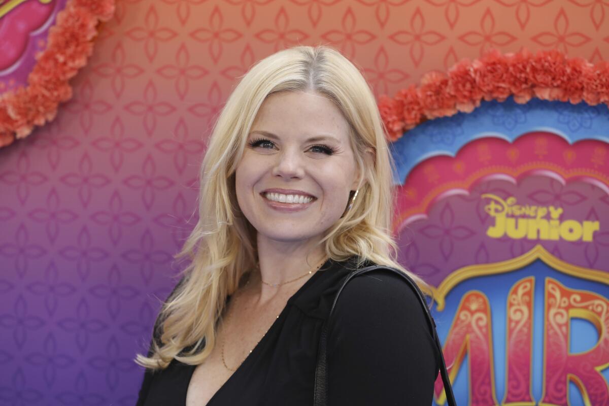 A woman with blond hair wearing a black dress smiles for cameras