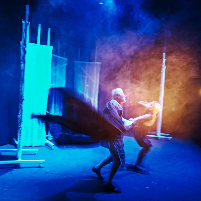Two actors in mist and blue light onstage. 