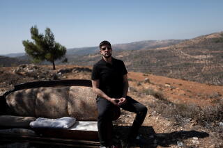 A man in dark clothes poses near a couch in a spot overlooking his family's land