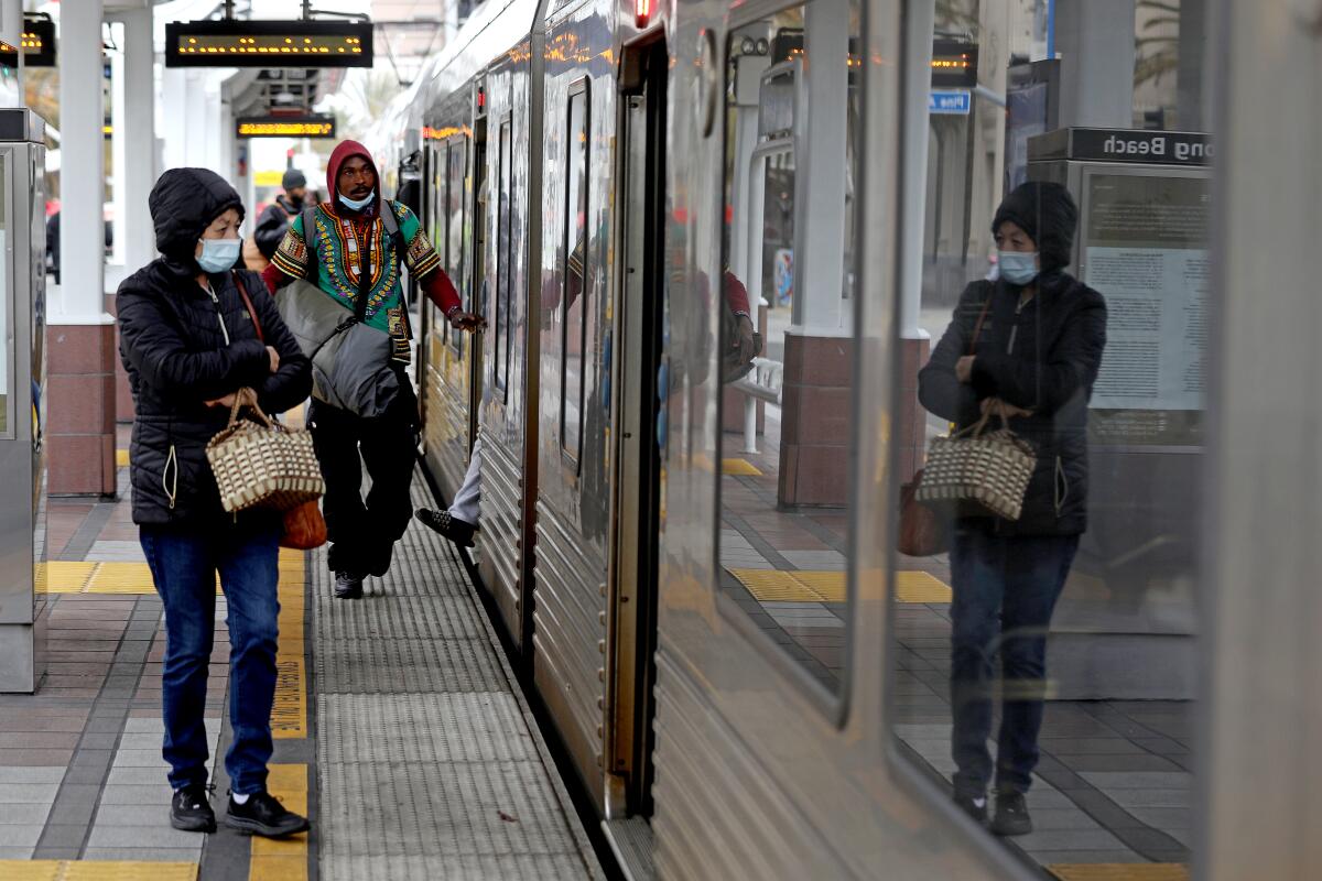 A woman is reflected in the window of a train as she and other passengers wait on a platform.