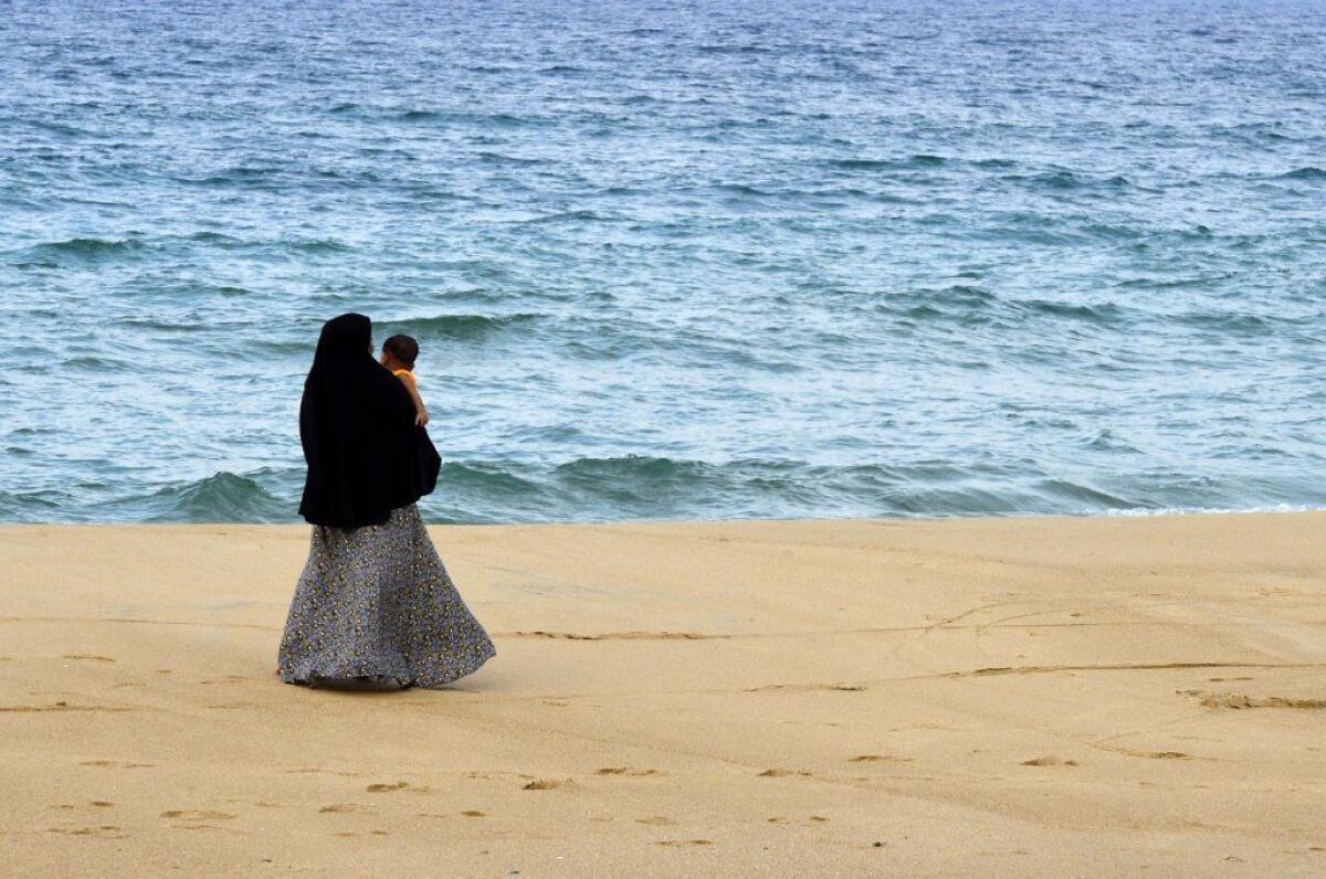 A Sri Lankan Muslim woman walks along a beach with her child in Kattankudy, the hometown of the alleged leader of the Easter bombings, Mohammed Zahran.