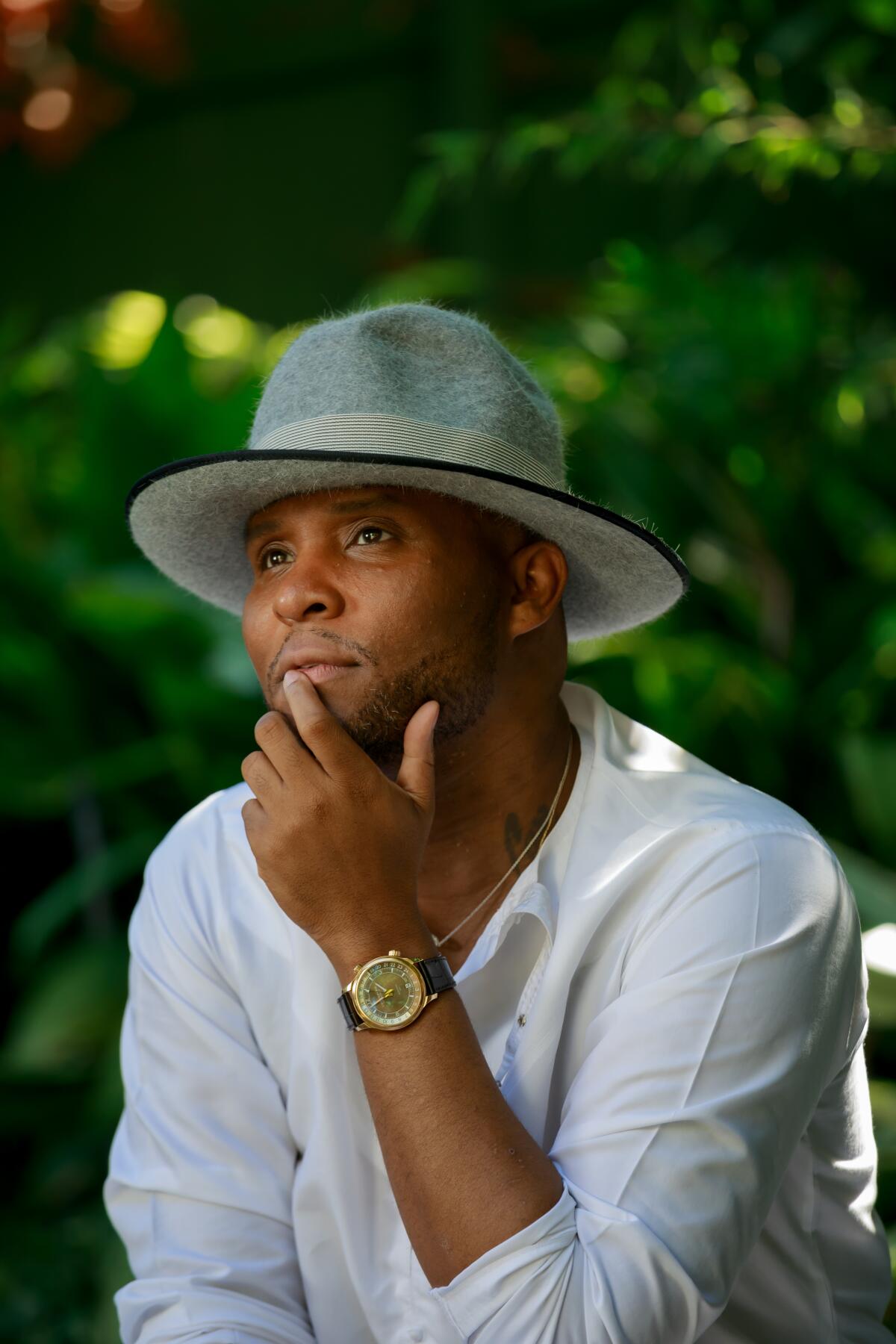 A man in a white shirt and hat places his hand on his chin