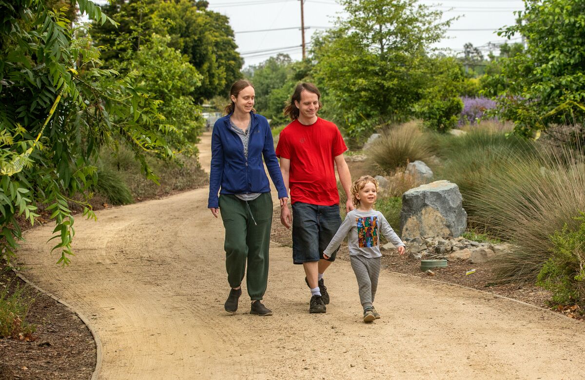 A couple walk with a 2-year-old child along a pathway on the north Westwood Greenway.