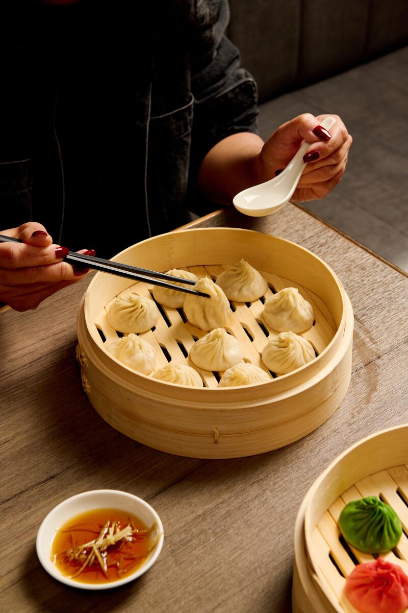 A person uses chopsticks to pick up a soup dumpling from a steamer basket.