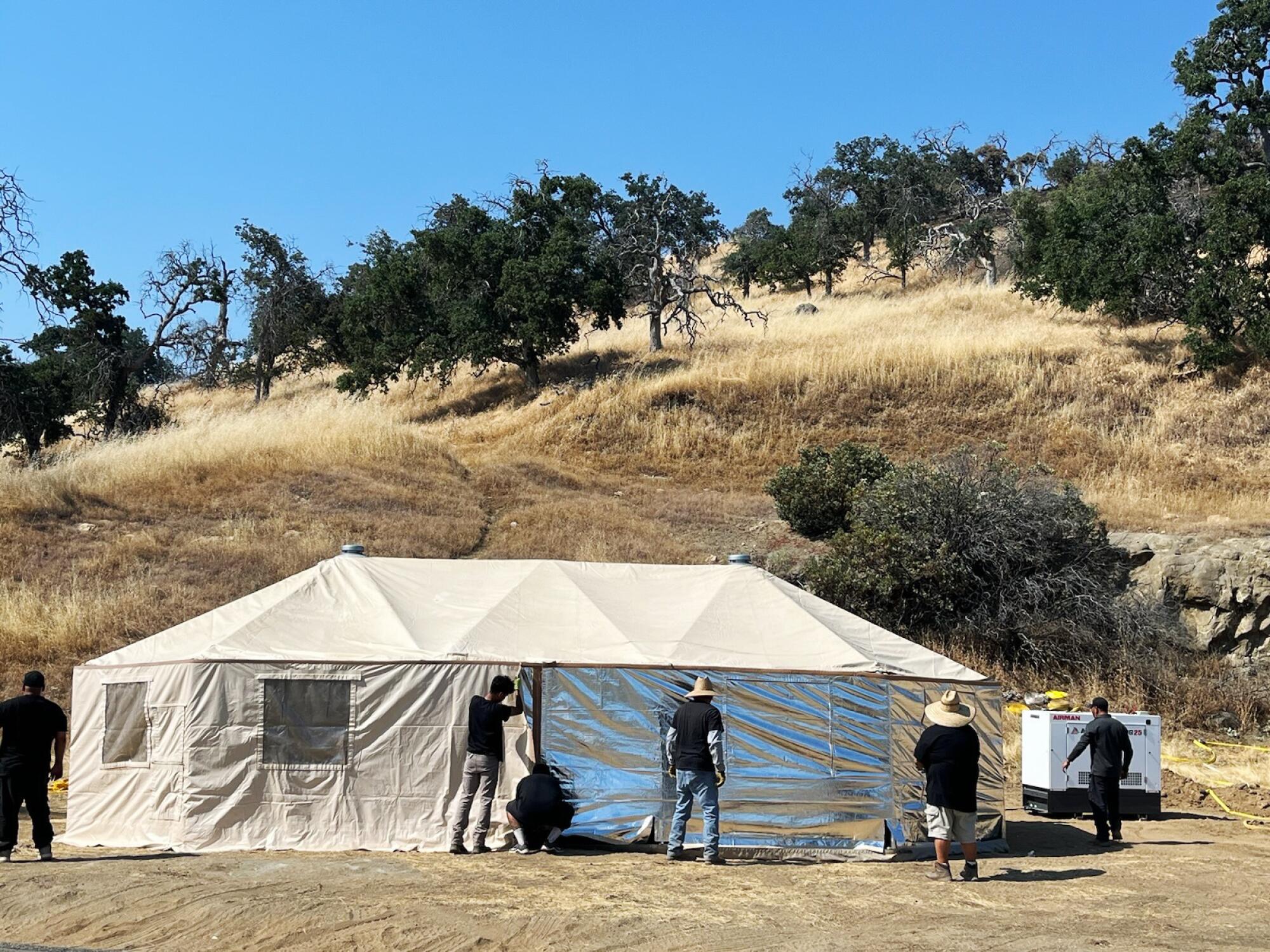 People stand next to an air conditioned yurt, which sits next to an oak-dotted hillside.