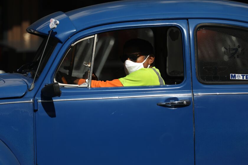 ORANGE, CA - JUNE 18: A man wearing a mask and driving a vintage VW Bug at the Orange Circle on Thursday, June 18, 2020 in Orange, CA. Gov. Gavin Newsom on Thursday ordered all Californians to wear face coverings while in public or high-risk settings due to coronavirus. Orange County recently did not require face mask to be worn. (Gary Coronado / Los Angeles Times)