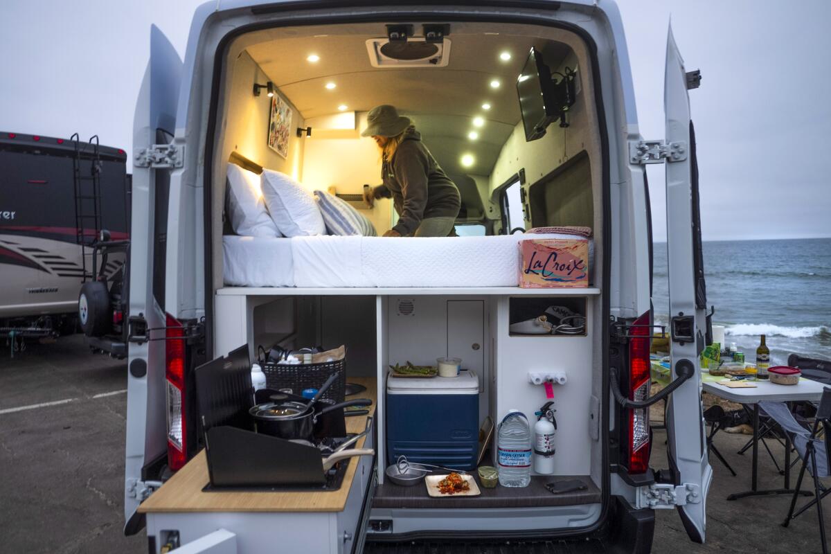 The back of a van shows a bed and compartments for cooking and food storage
