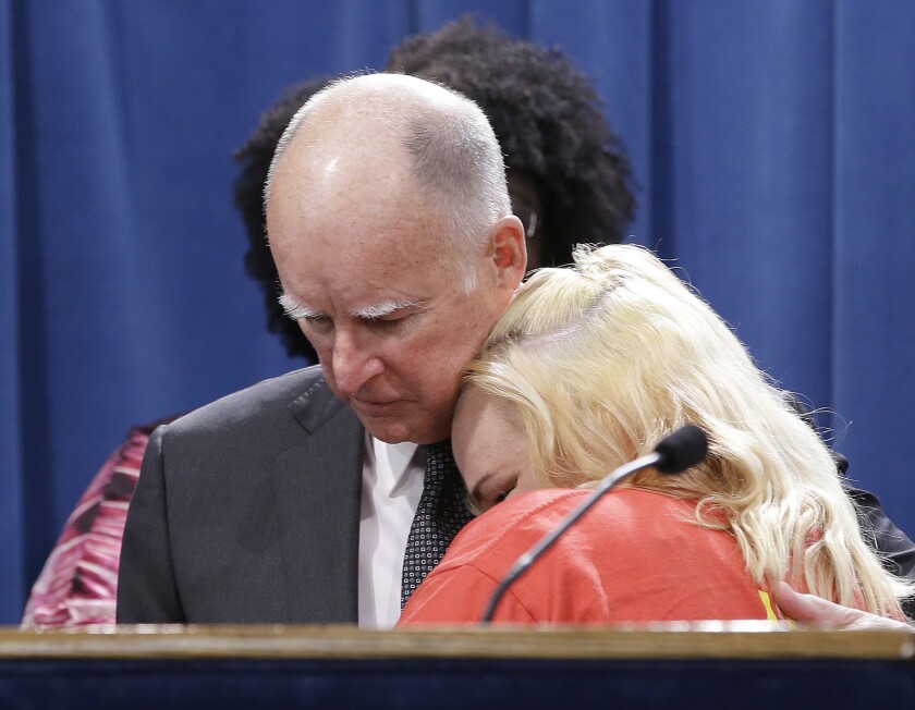 Gov. Jerry Brown is hugged by Holly Dias, a Burger King employee who praised Brown's announcement of proposed legislation to increase the state's minimum wage to $15 per hour by 2022, during a news conference in Sacramento on Monday.