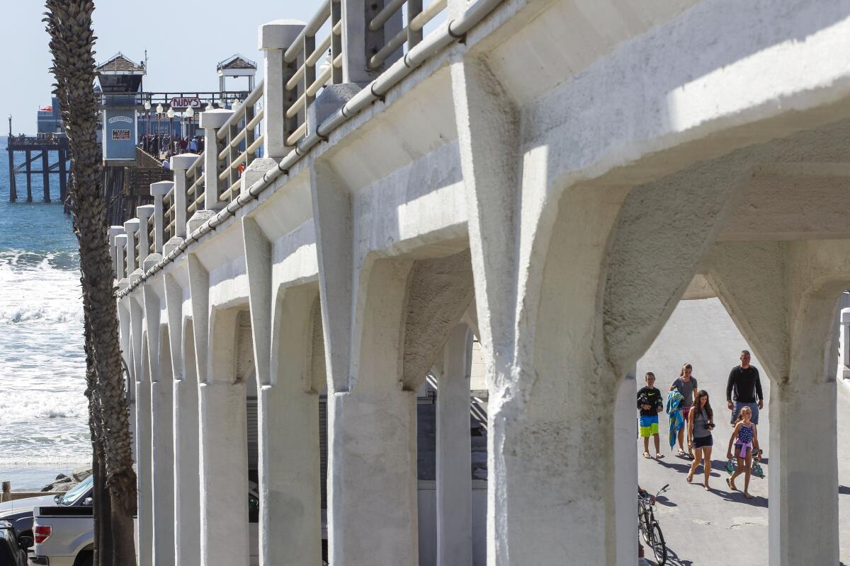 With the concrete bridge that connects to the Oceanside Pier in the foreground, people walk down ramp to The Strand in 2018.