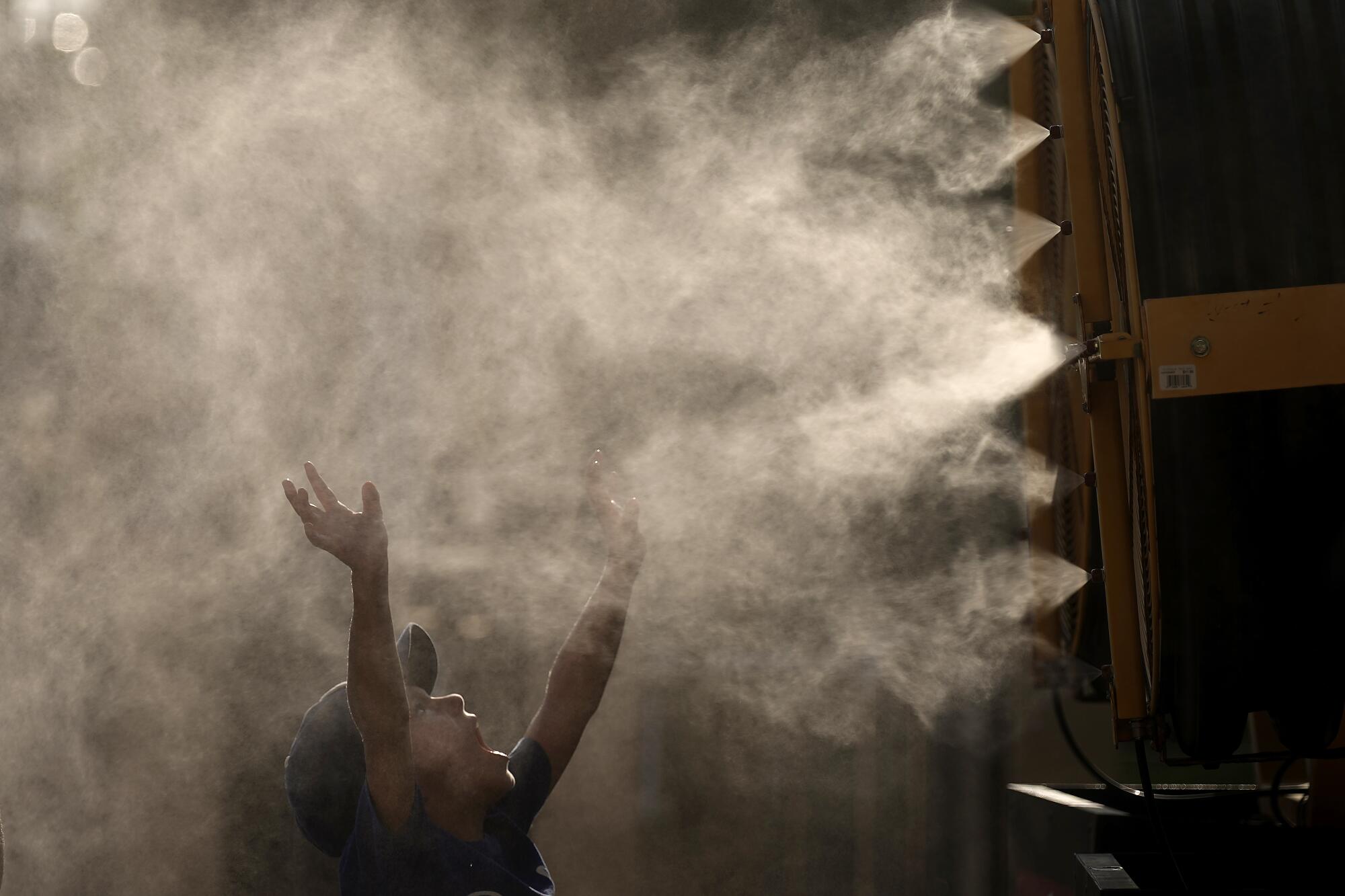一个小男孩举起双手，张开嘴，雾气从一系列喷嘴中喷出。