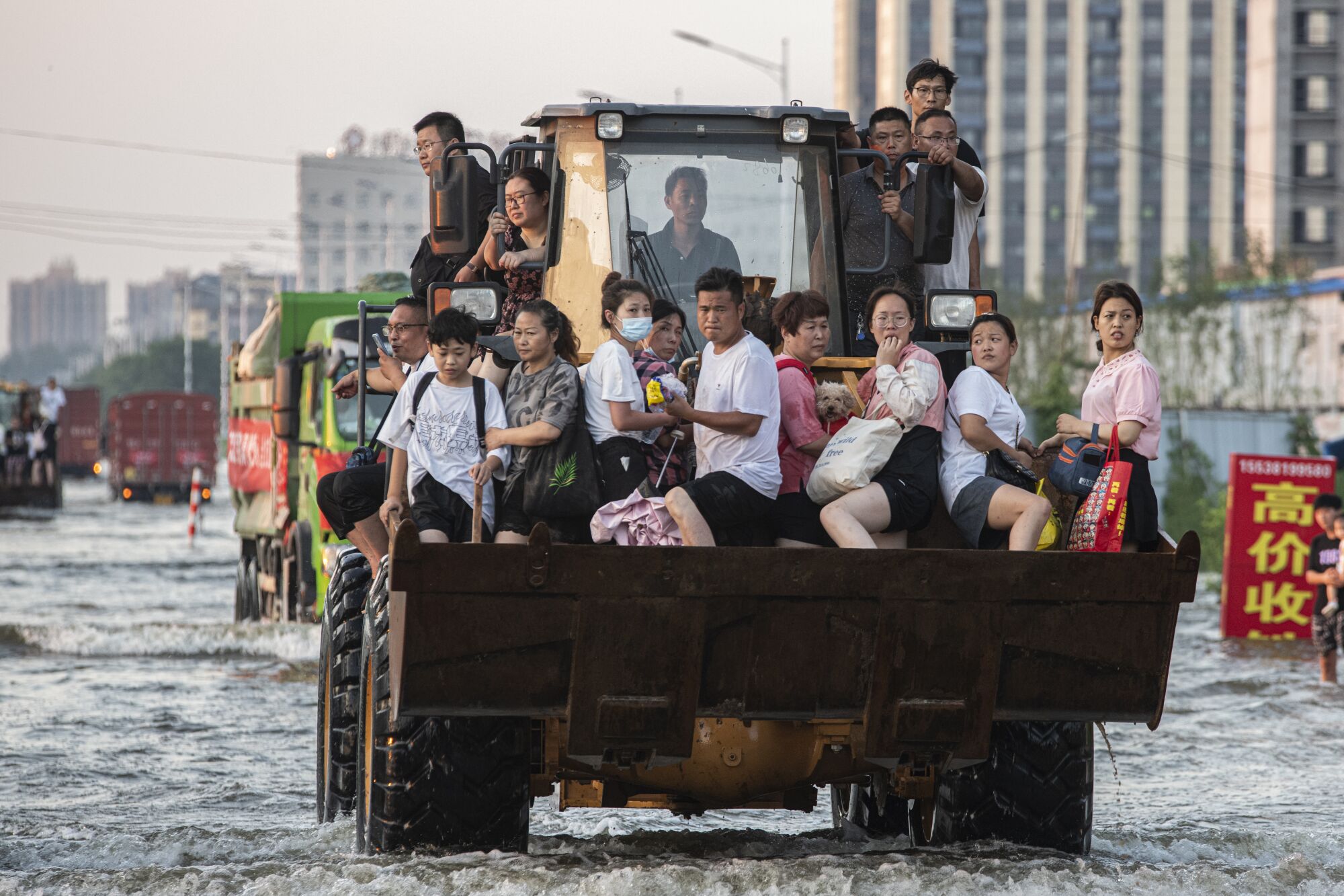 People sit in a bulldozer navigating flooded streets 