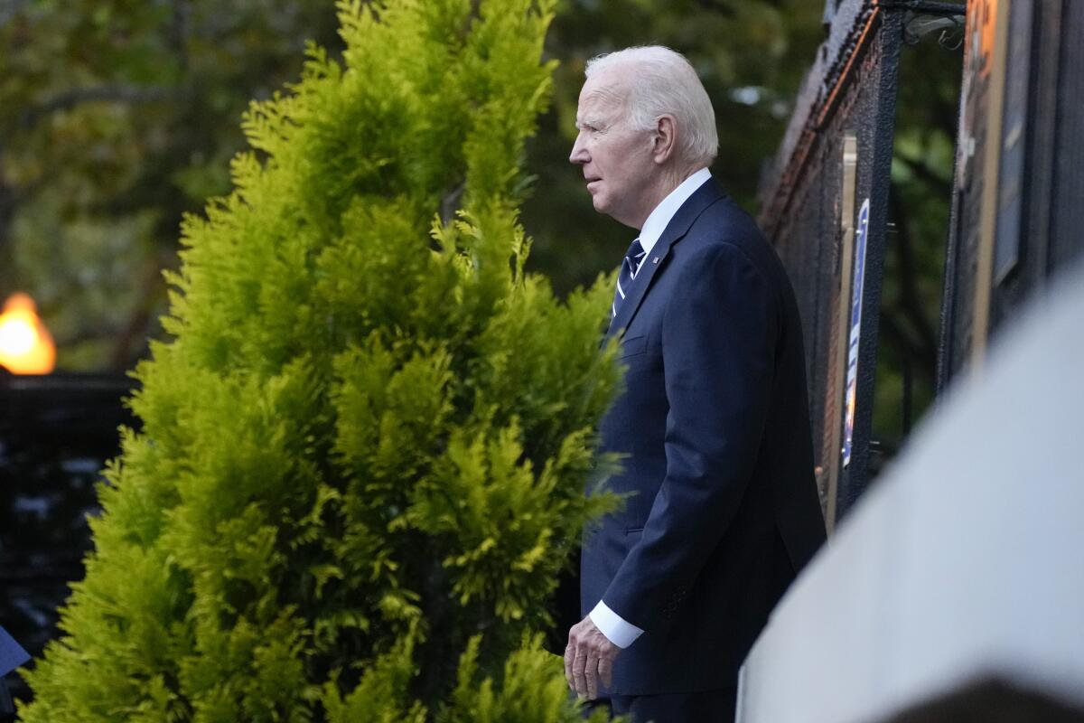 President Biden walks out of a building and past trees.