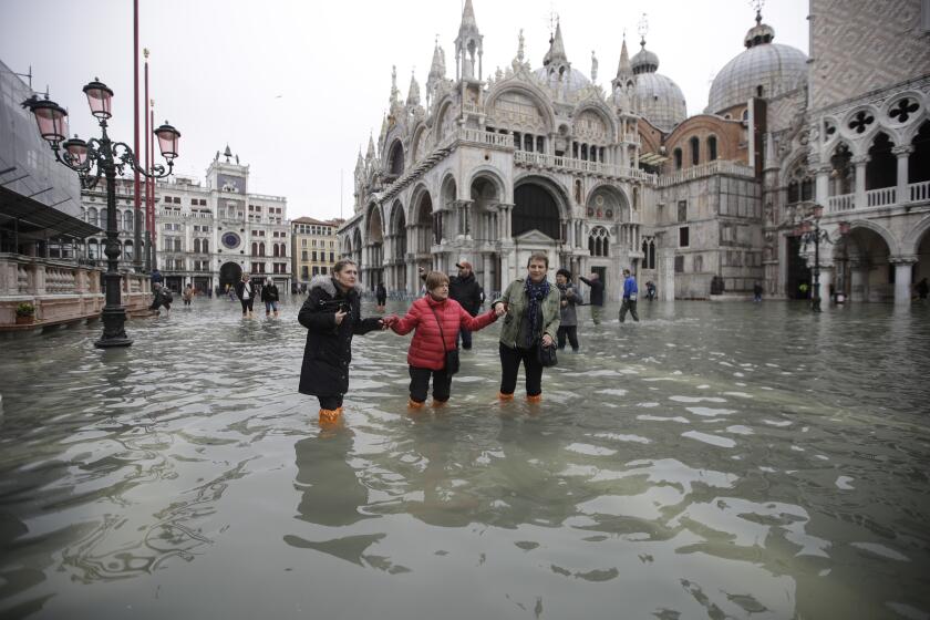 People wade through water in a flooded St. Mark's Square in Venice, Italy, Wednesday, Nov. 13, 2019. The high-water mark hit 187 centimeters (74 inches) late Tuesday, Nov. 12, 2019, meaning more than 85% of the city was flooded. The highest level ever recorded was 194 centimeters (76 inches) during infamous flooding in 1966. (AP Photo/Luca Bruno)
