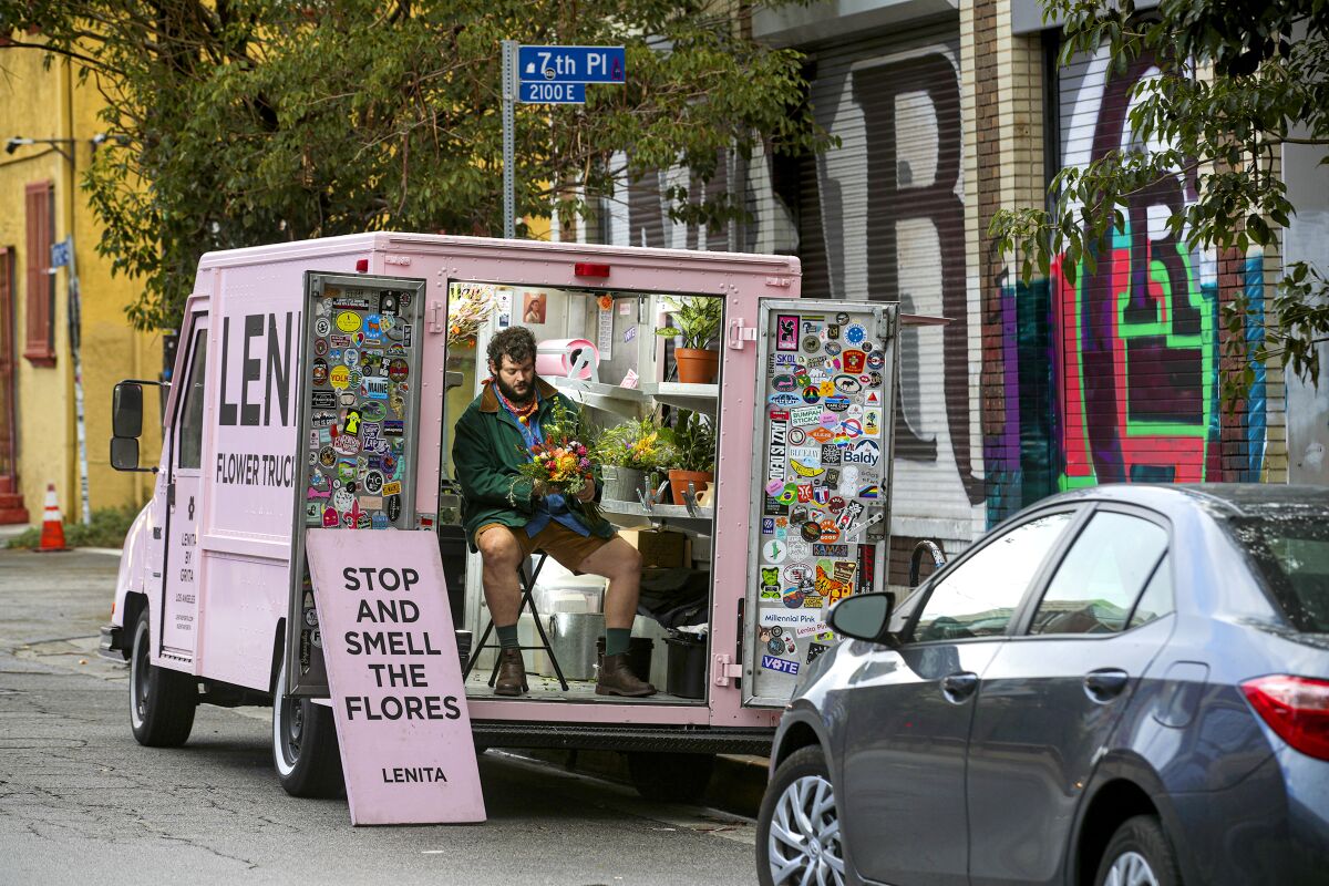 The florist sits in the back of his pink truck. A pink sign reads "Stop and smell the flores."