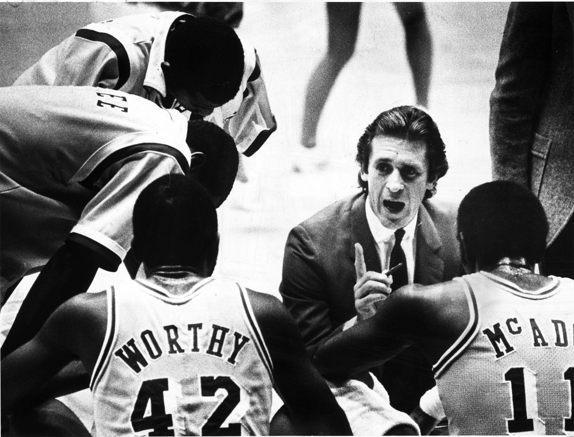 A man in a suit with slicked-back hair instructs Lakers players during a timeout