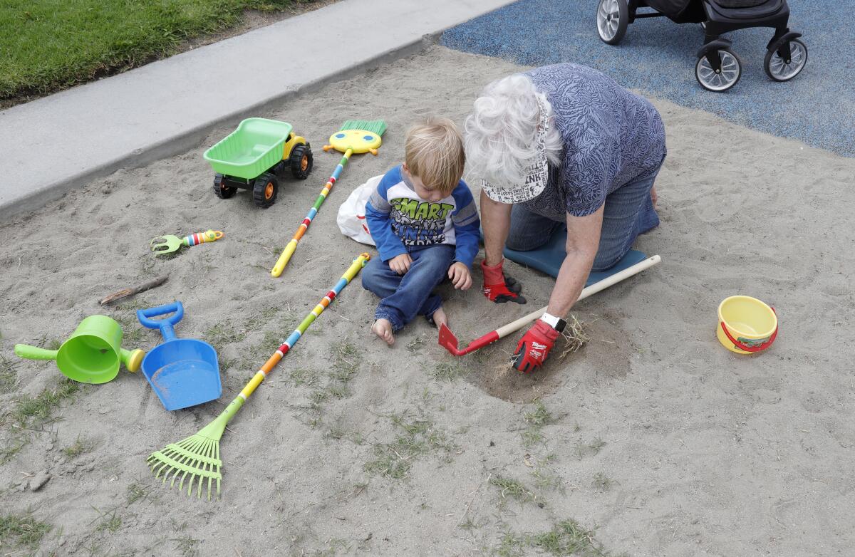 Maureen Farsadi, right, and 2-year-old Dylan Bruno pull small weeds from the playground at Golden View Park on Monday.