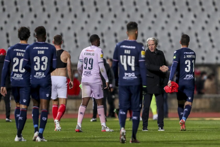 Benfica coach Jorge Jesus shakes hands with Belenenses' Joao Monteiro, right, a goalkeeper who had to start as a field player, at the end of the Portuguese Primeira Liga soccer match between Belenenses SAD and SL Benfica, Saturday, Nov. 27, 2021. Belenenses SAD started the match with only nine players due to a coronavirus outbreak. Portuguese health authorities on Monday, Nov. 29, 2021, identified 13 cases of omicron, the new coronavirus variant spreading fast globally, among members of Belenenses SAD. (AP Photo/Pedro Rocha)