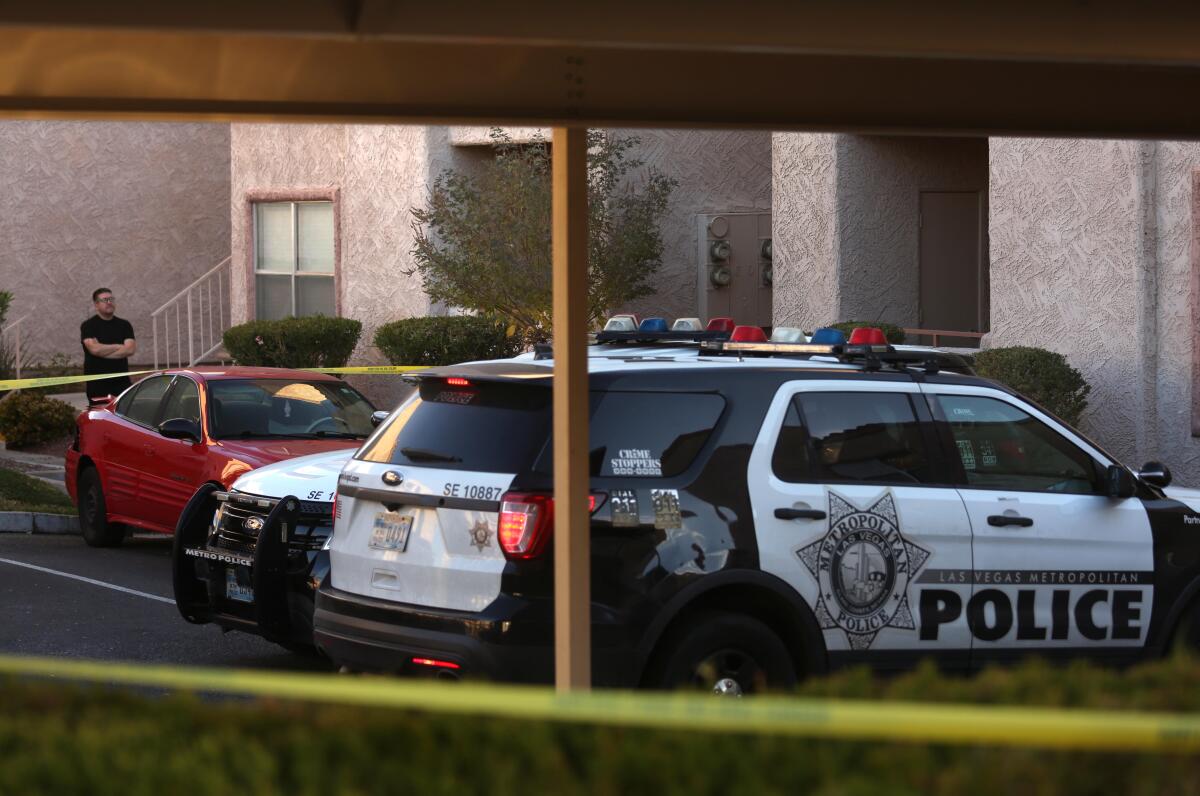 A man with his arms crossed stands outside police tape in an apartment complex parking lot with patrol SUVs