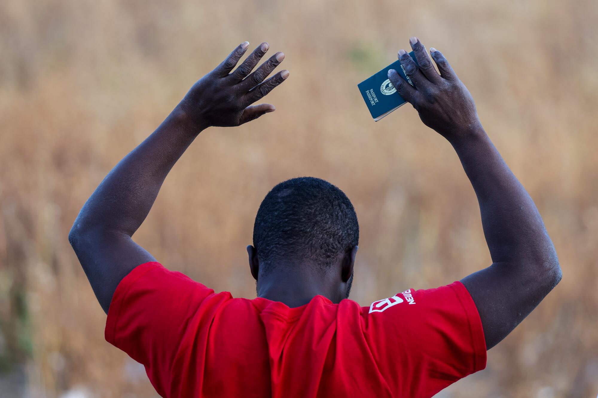 A man standing in a field raises his arms with his passport in his right hand