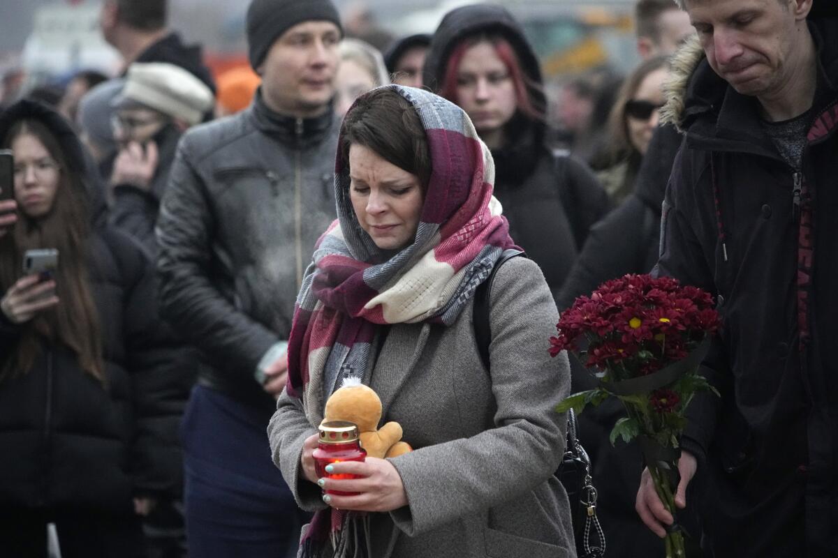 A woman bundled against the cold holds a toy and candle amid a group of people, some holding flowers. 