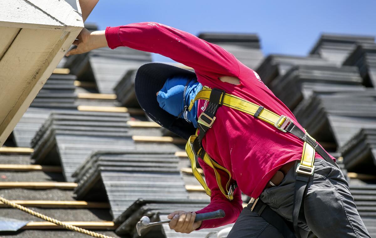 A man works on a roof while he protects his face from the blazing sun with a hat and a mask.