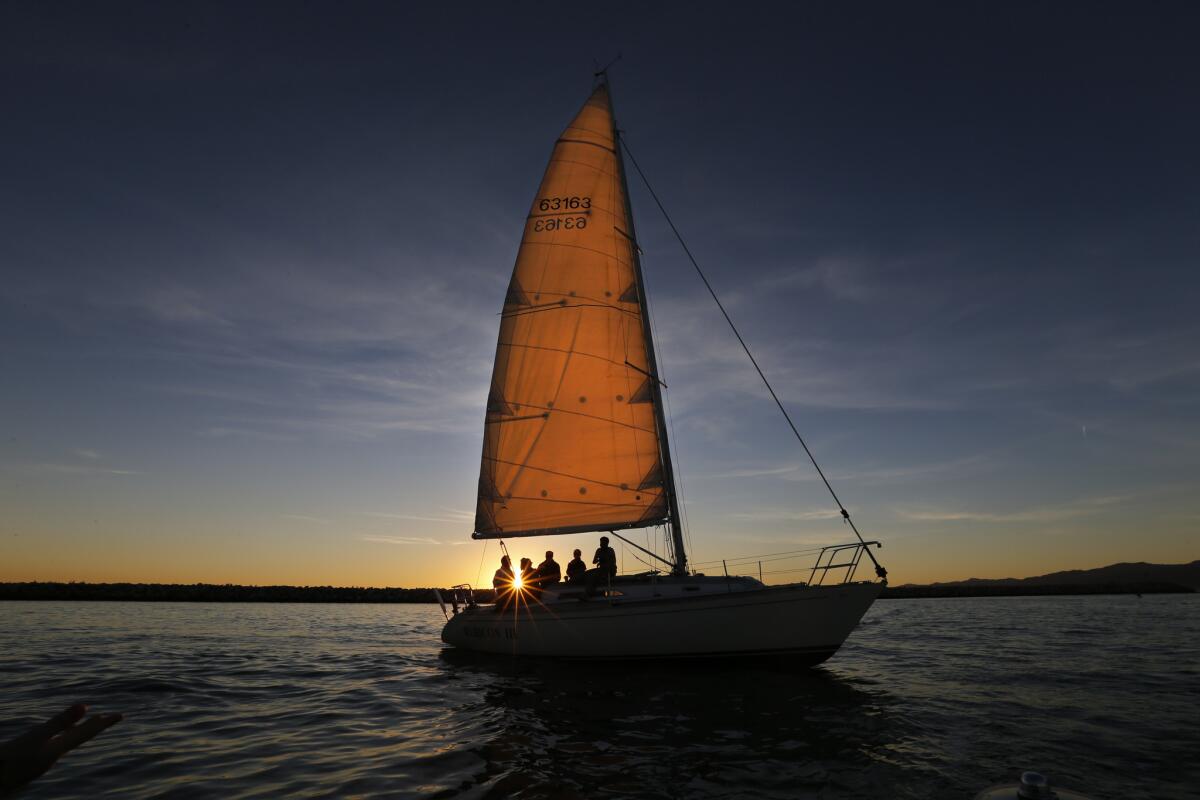 The sunset illuminates the sail as a crew of sailors glides across the water in Marina del Rey. Residents are at odds with Los Angeles County officials over a planned hotel development.