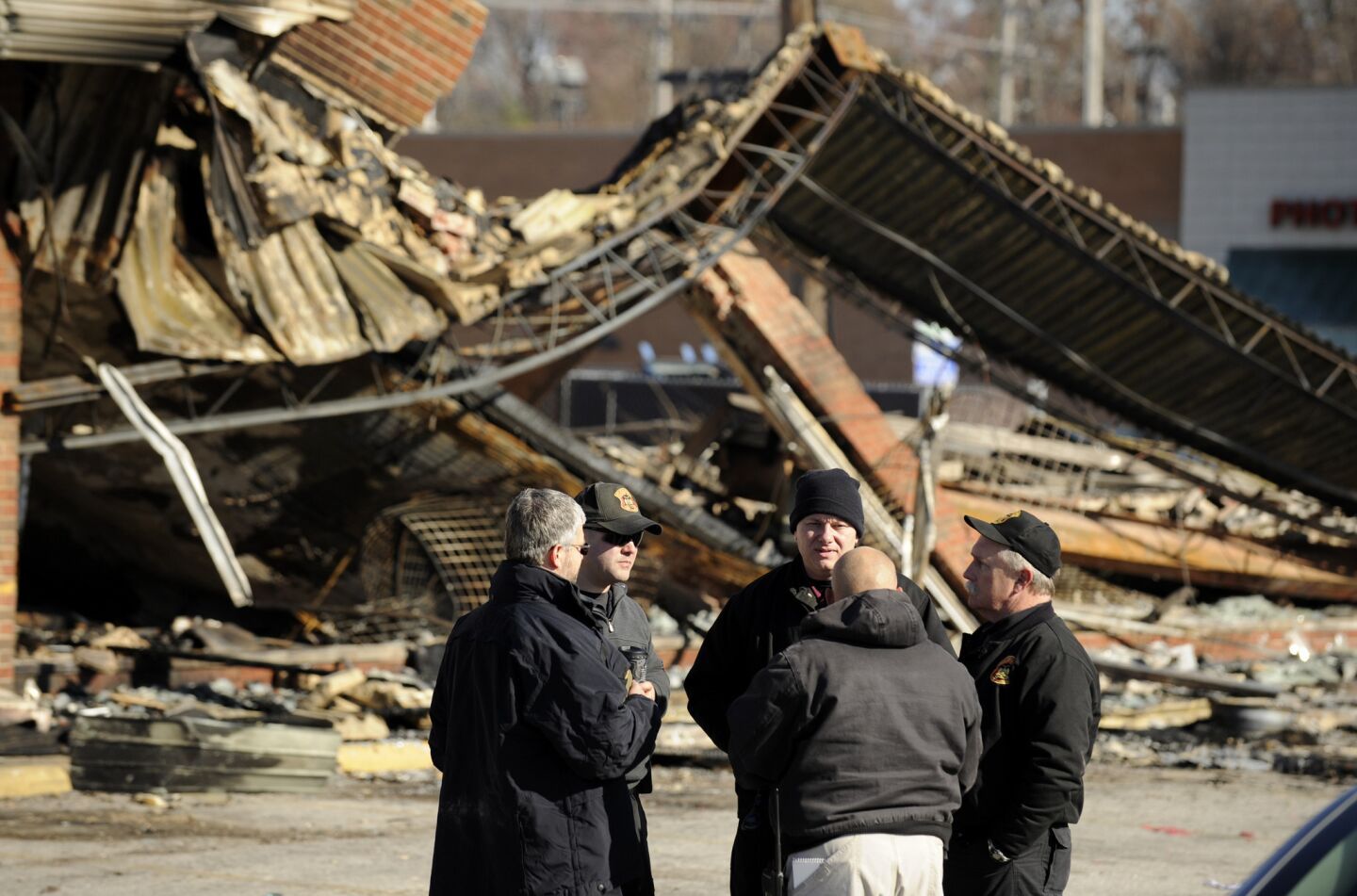 Police investigators meet in front of a burned strip mall at Chambers Road and West Florissant Avenue in Ferguson, Mo.