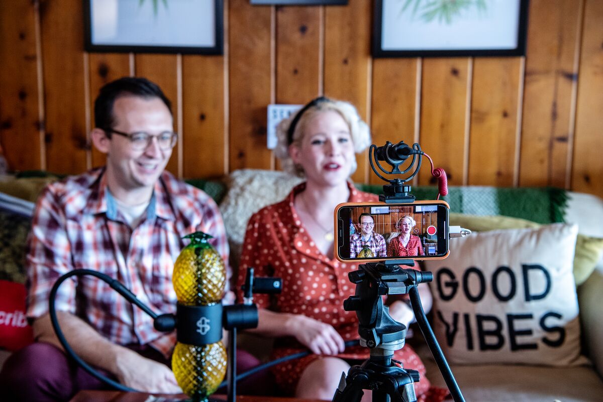 Two people sitting on a couch with video-recording equipment in the foreground