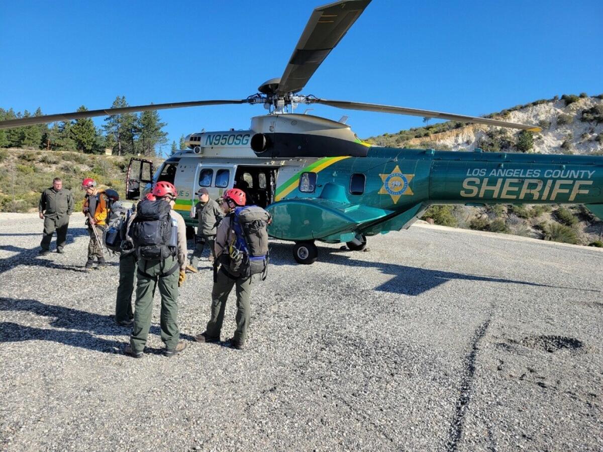 Rescue workers with helmets and backpacks stand next to a helicopter