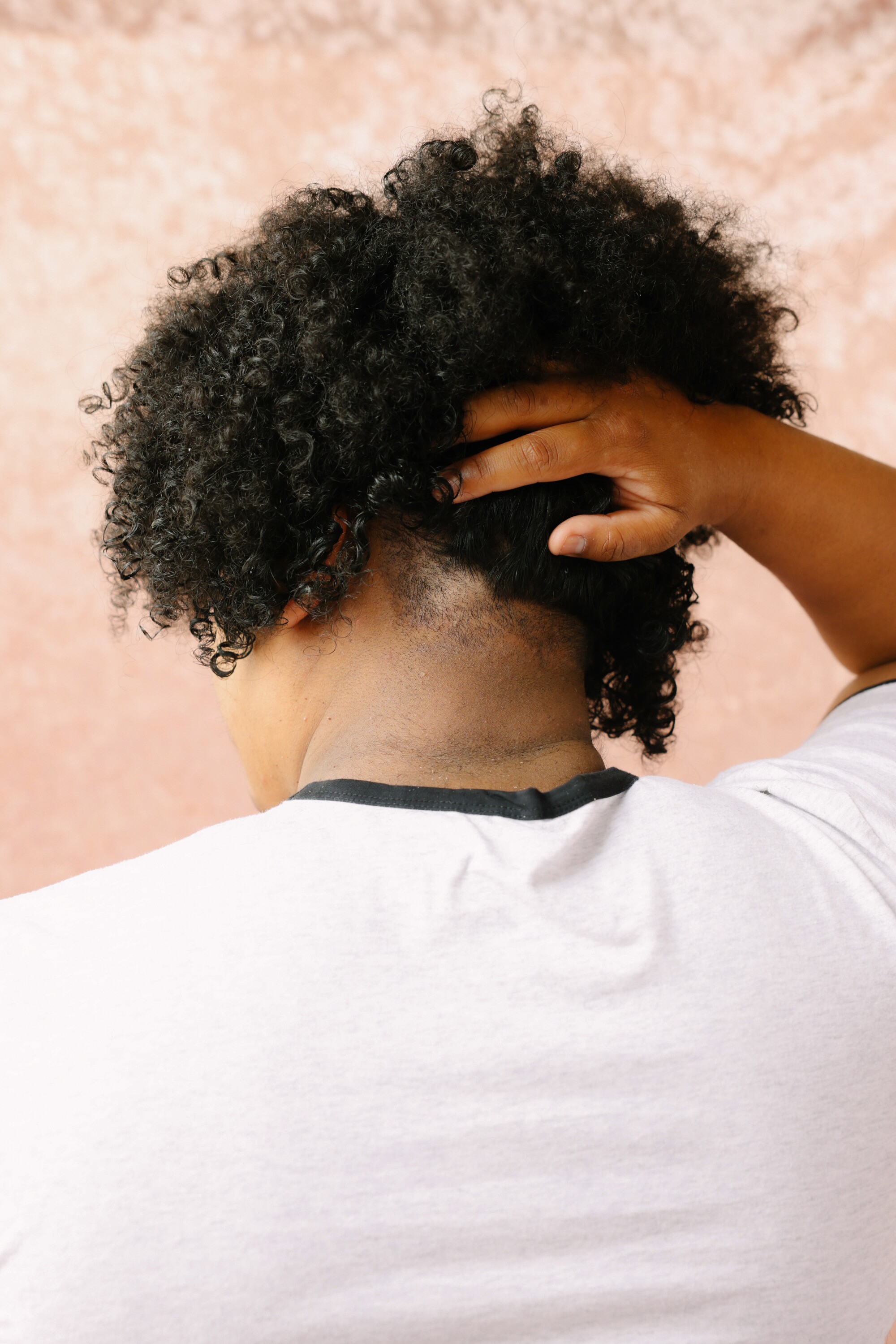 A person's back is visible;  They lift their hair to reveal a small shaved patch 