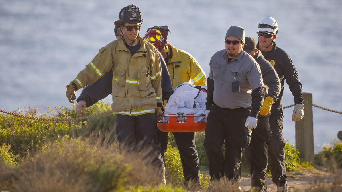 San Diego firefighters help carry the bodies of two paragliders who collided on a cliff at the Torrey Pines Gliderport on Saturday.
