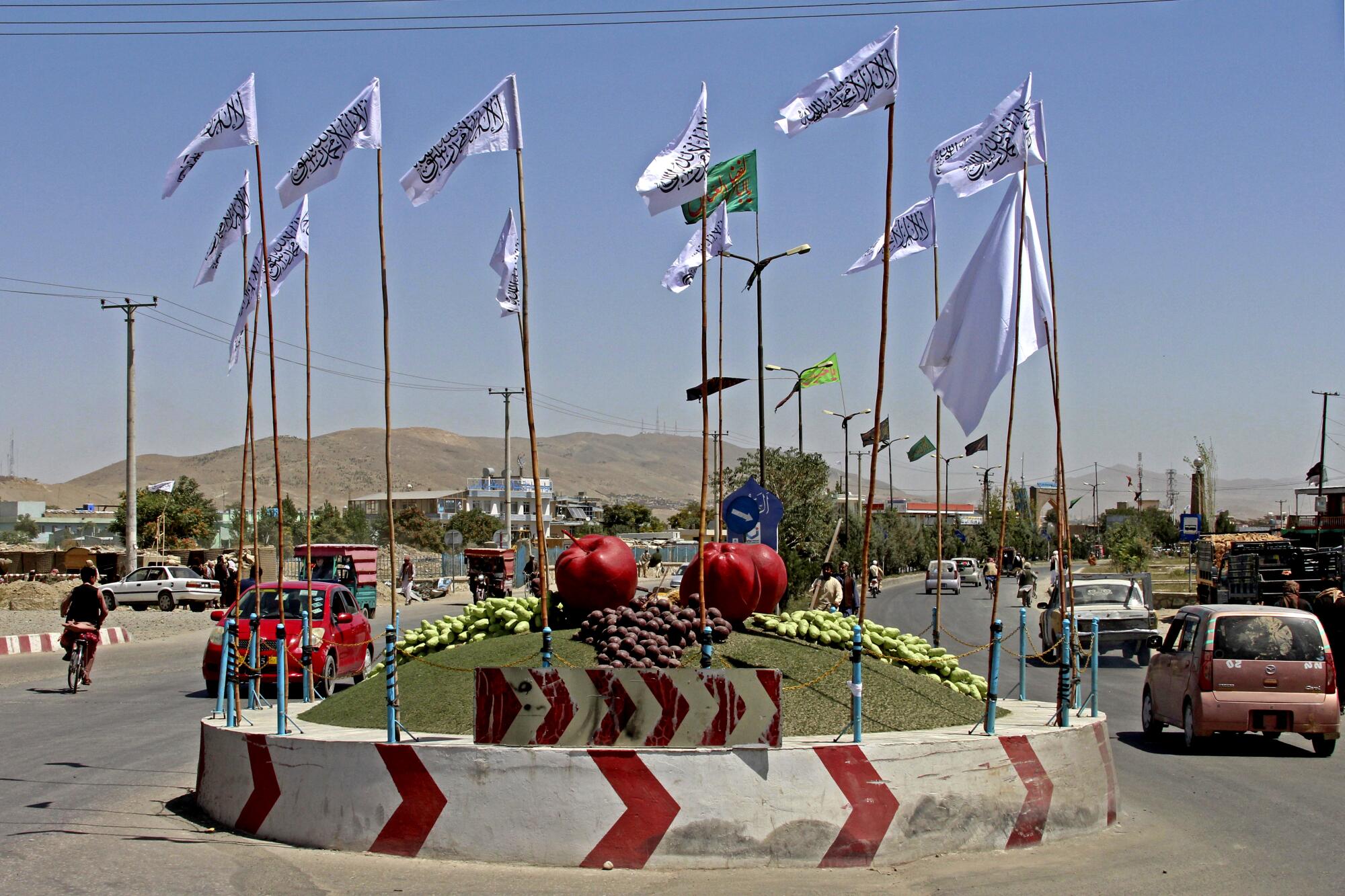 White Taliban flags surround a traffic circle that is decorated with sculptures of fruit