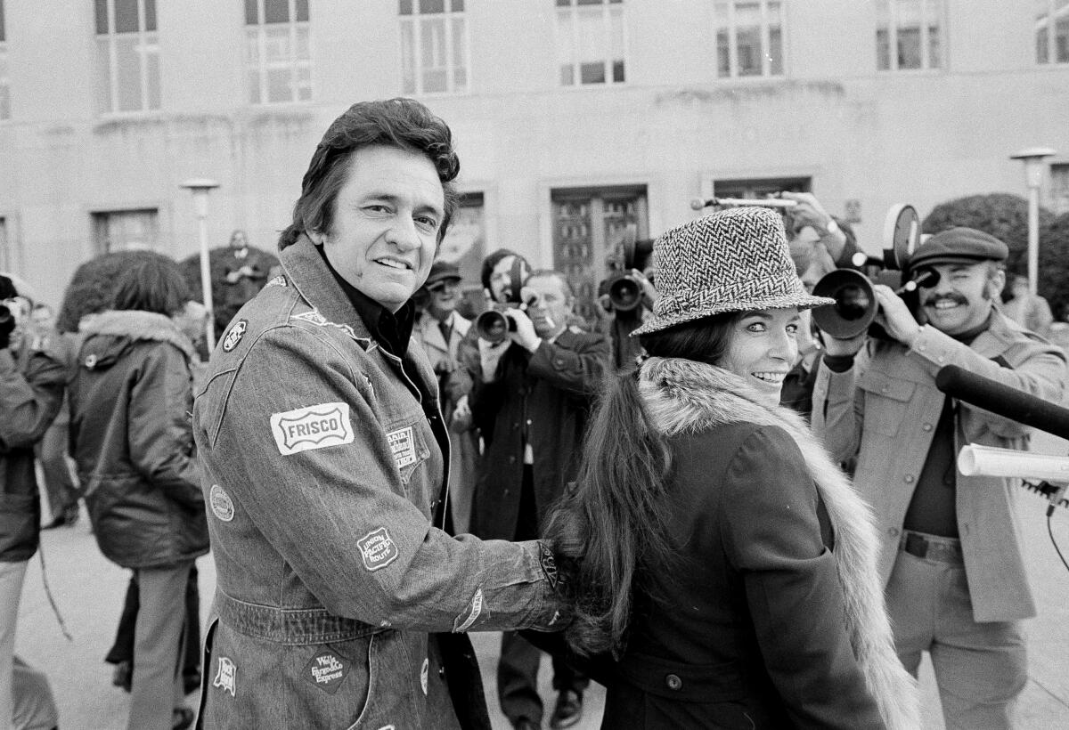 Johnny Cash and June Carter Cash walk toward a crowd outside a building in a black-and-white photo