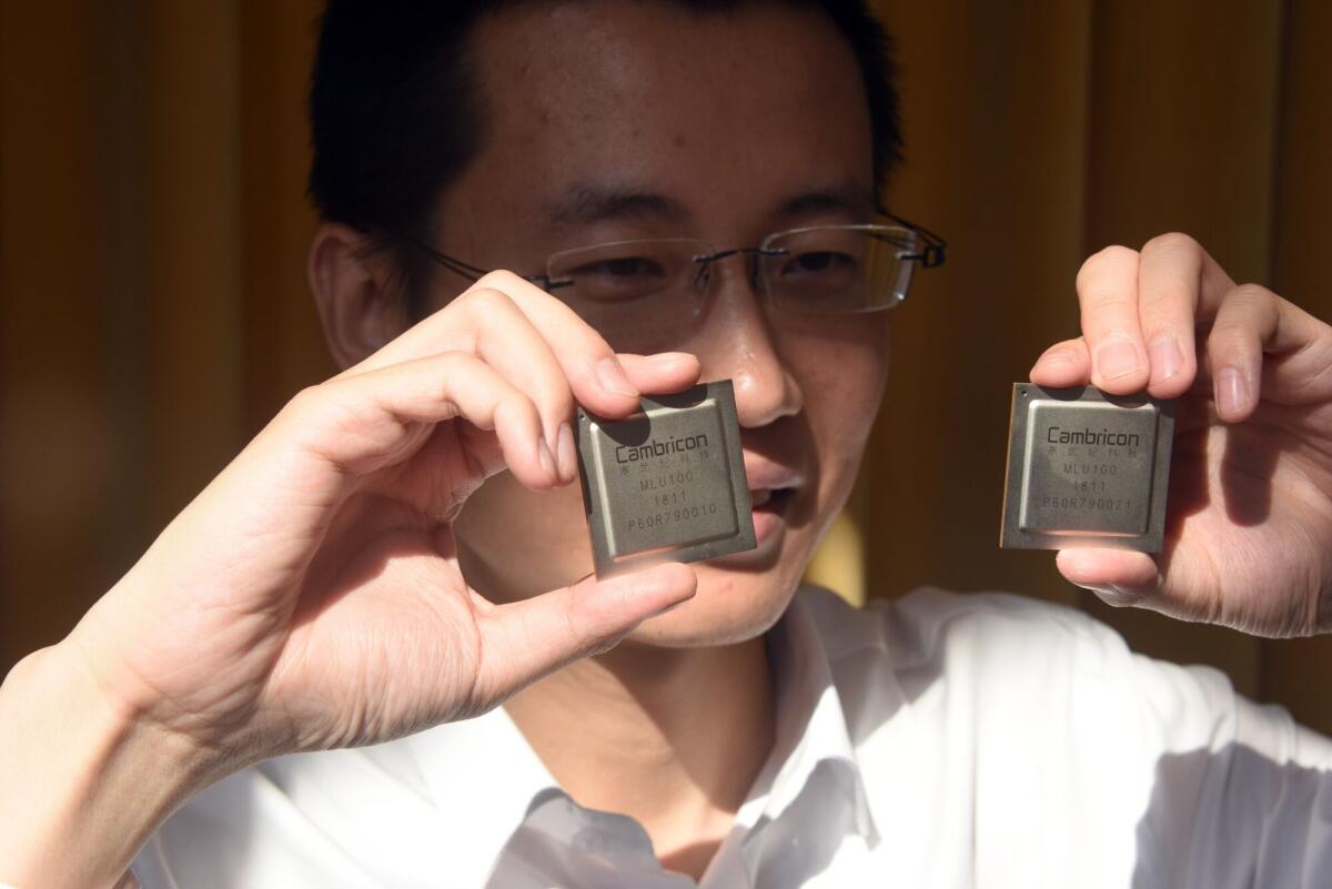 A man with dark hair and glasses, holding up a square chip in each hand