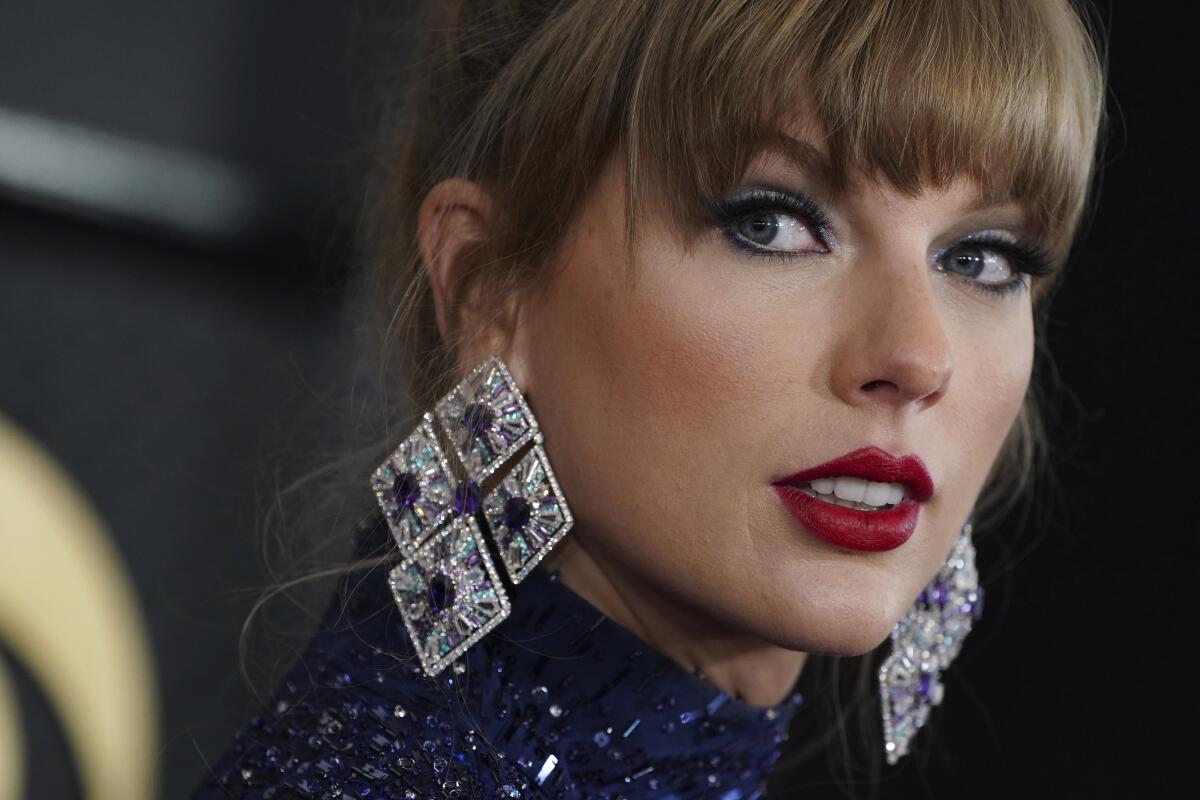 Taylor Swift with bangs wearing large jeweled earrings and red lipstick. 