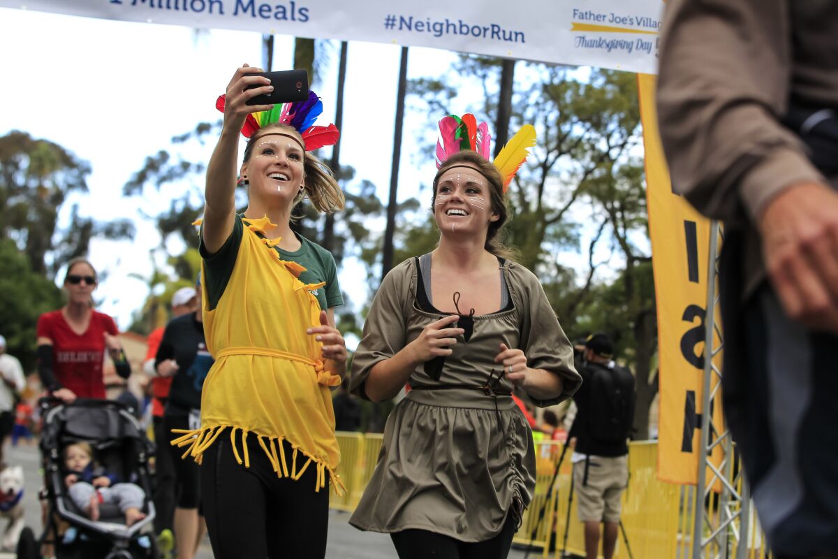 Tori Light (left) and Beki Turlay shoot a photo as they cross the finish line during the Father Joe's Villages Thanksgiving Day 5k in San Diego.