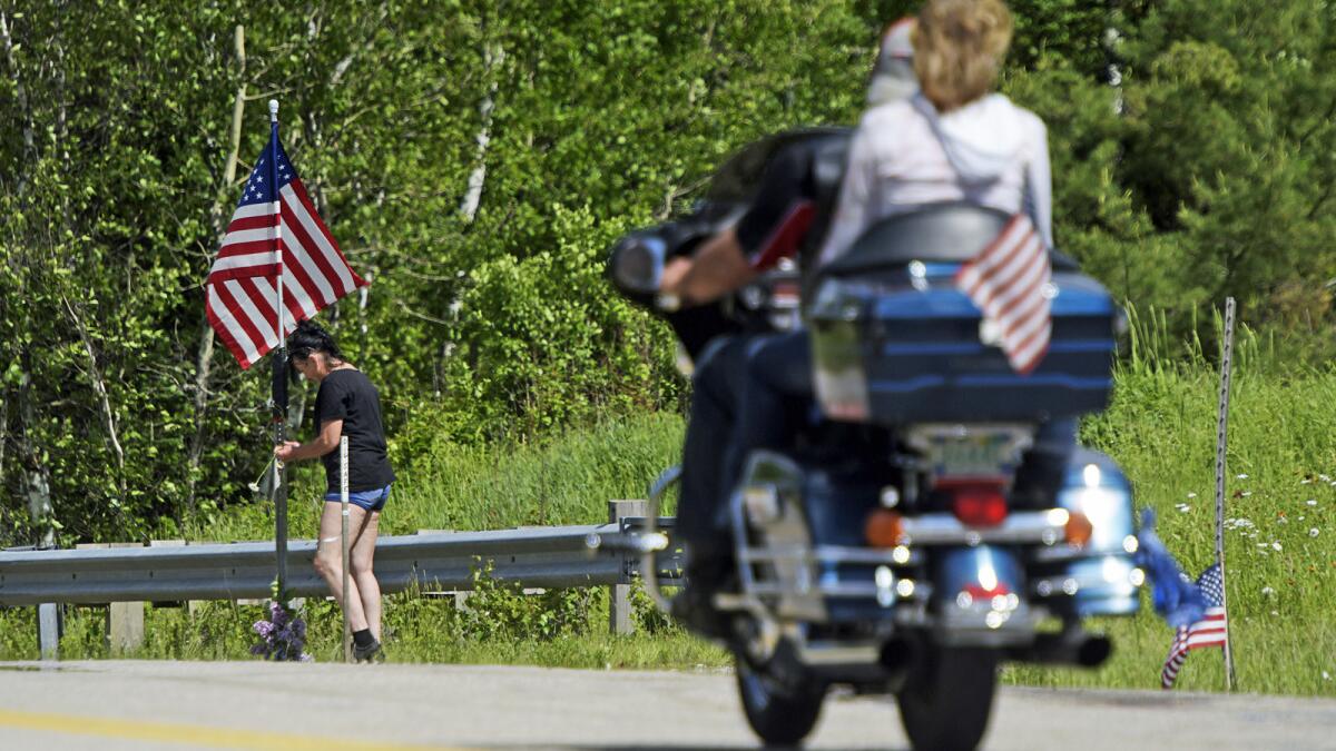 A motorcycle passes as a woman leaves flowers at the scene of the fatal accident on Route 2 in Randolph, N.H., Saturday.