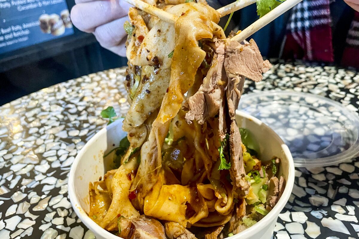 chopsticks lift noodles and lamb from a bowl 