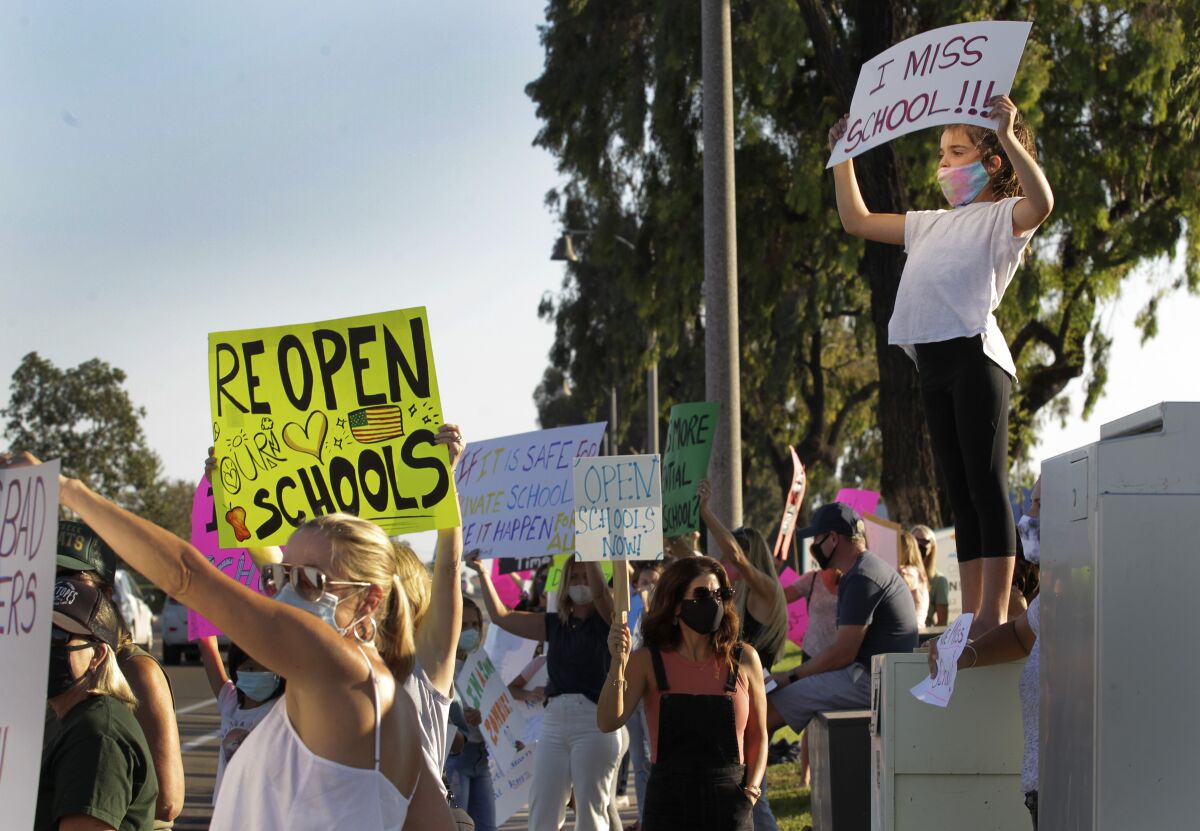 Penelope Reiss, 8, right, displays a sign to open schools during a protest Wednesday at Carlsbad School district.