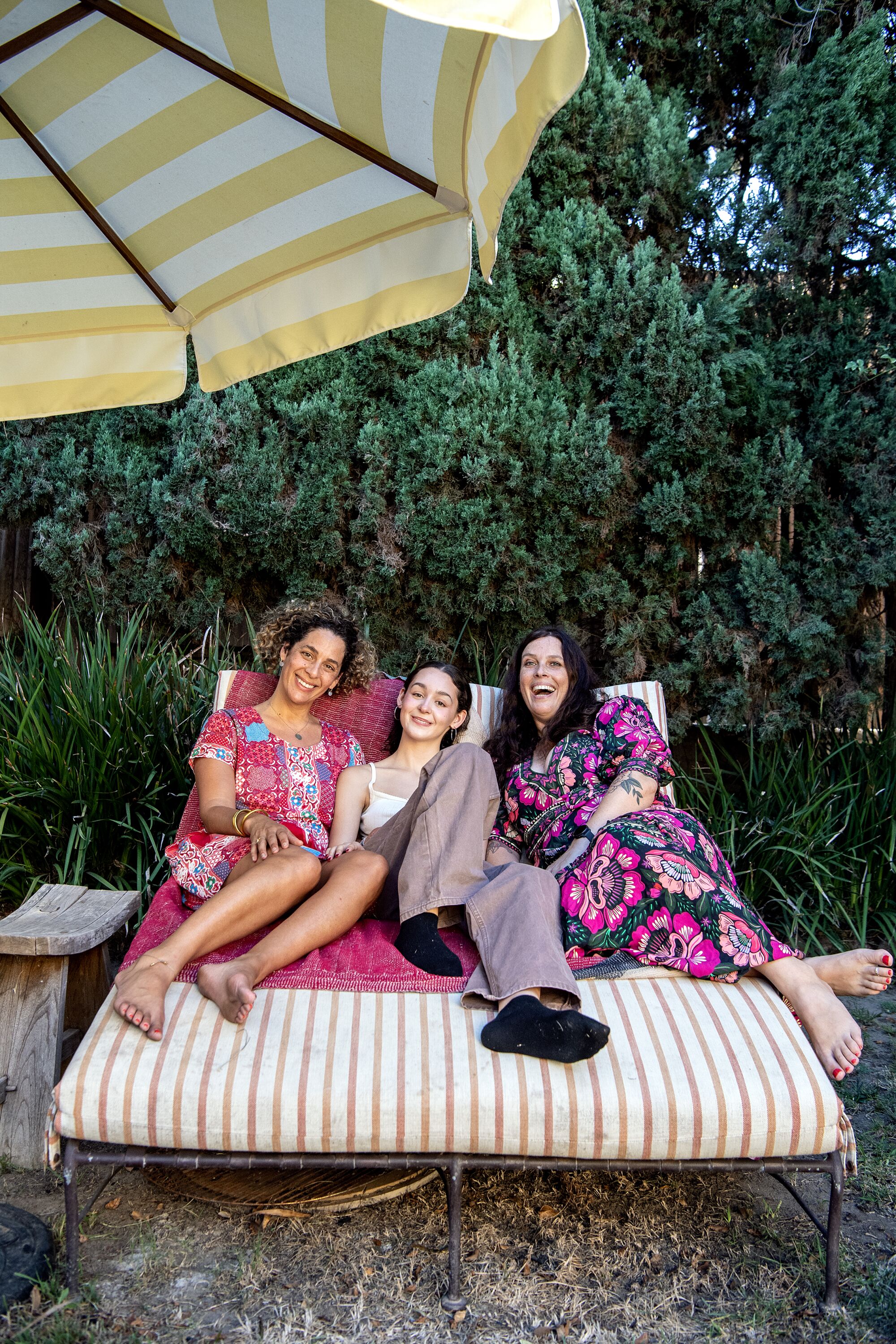 Three women reclining on a lounge chair outside.