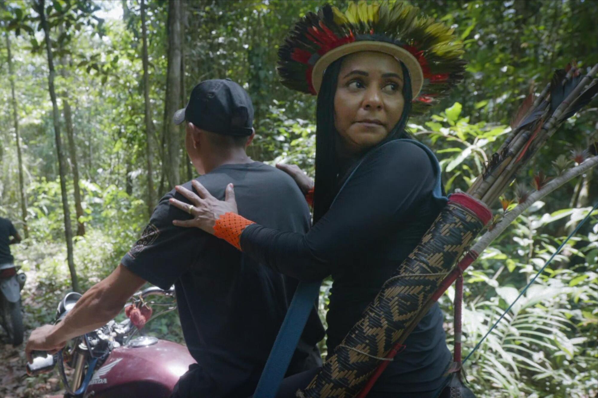A woman activist rides on the back of a motorcycle in the Amazon rainforest.