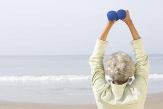 Senior woman exercising with dumbbells on beach.